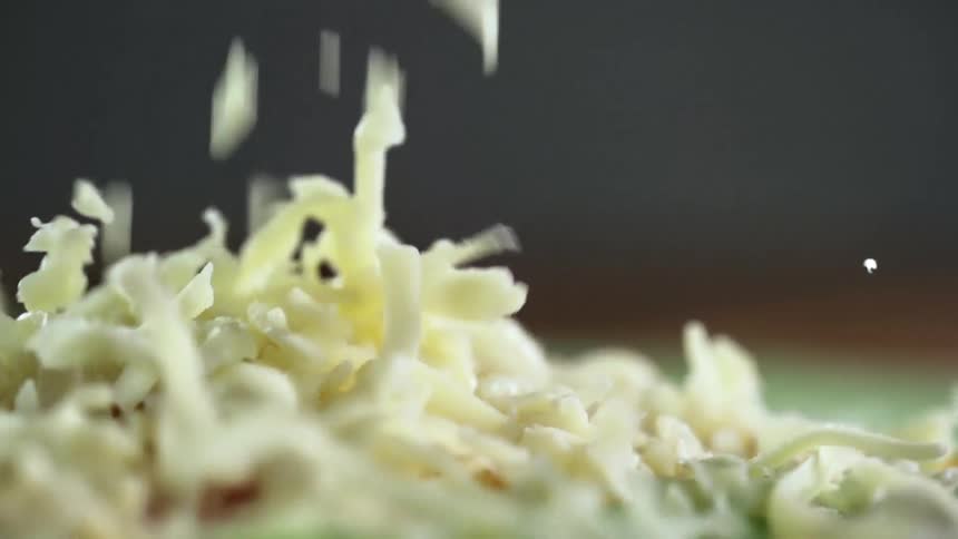 Grated white cheese falls over a green flour tortilla
