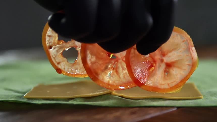 A gloved hand places tomato slices on to cheese slices on an herb wrap