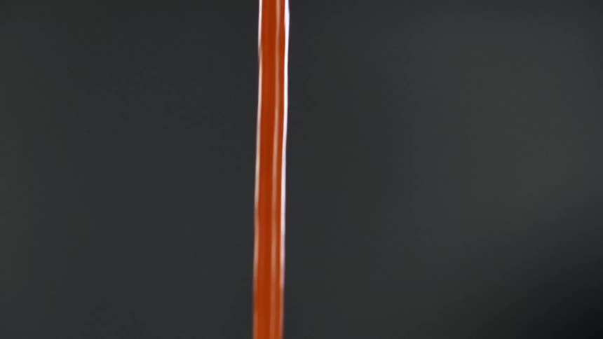 Red liquid pouring down in a single stream against a grey background