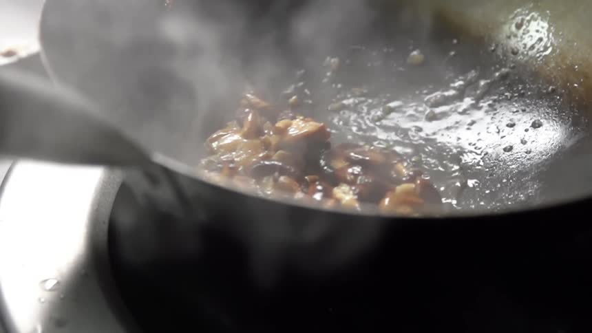 Shiitake mushrooms are stirred and cooked in a wok over a stove burner
