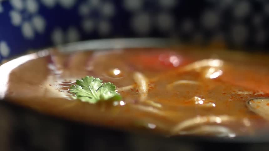 A single leaf of parsley is dropped onto the top of a asian soup in a ceramic bowl