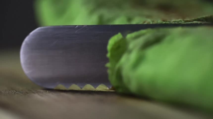 A serrated knife cuts through a green food item