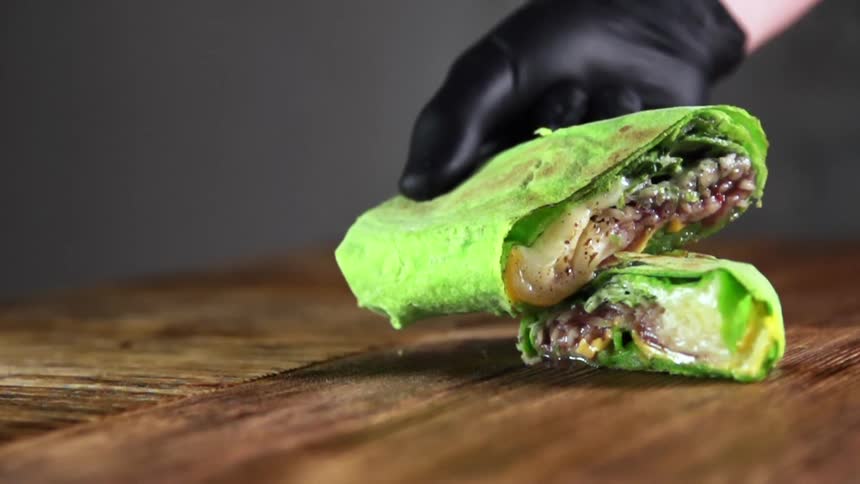 A person with black gloves placing a vegetable wrap on a table