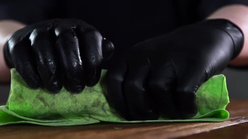 Food being tightly wrapped in a green tortilla by a cook wearing black gloves