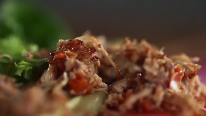 Shredded chicken is dropped onto a plate of vegetables