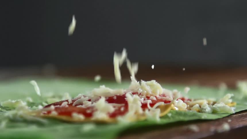 Shredded cheese being dropped onto food sitting on a table