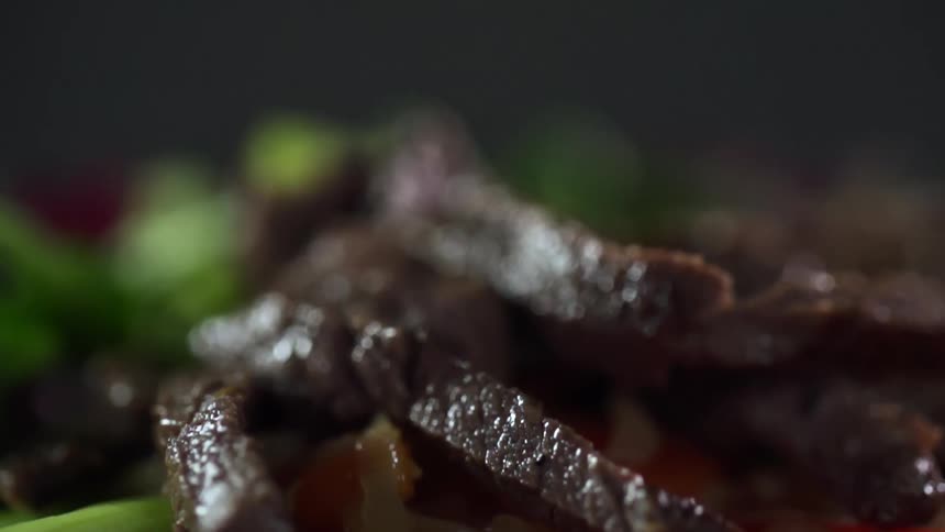 Strips of steak dropping over a plate of noodles with vegetables