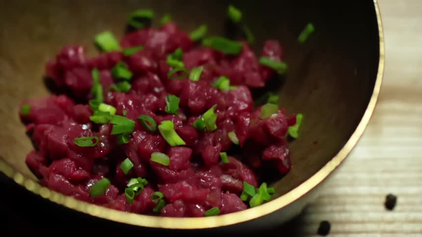 Sliced green onions fall into wooden bowl with chopped tuna