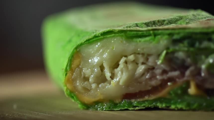 A spinach wrap filled with vegetables sits on a wood cutting board