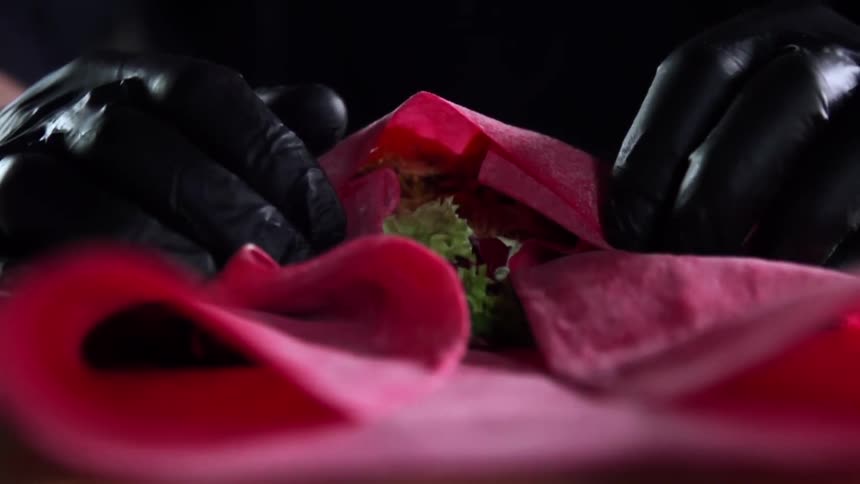 Black gloved hands fold and roll bread and fresh greens into a wrap