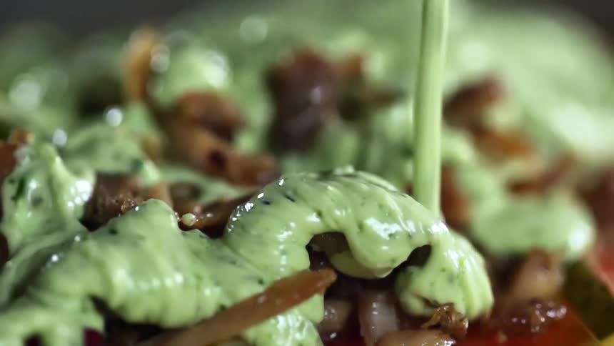 Green cream sauce being poured onto meat