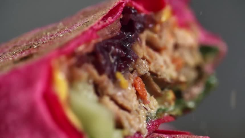 A wrap with meat and vegetables with seasoning falling on it