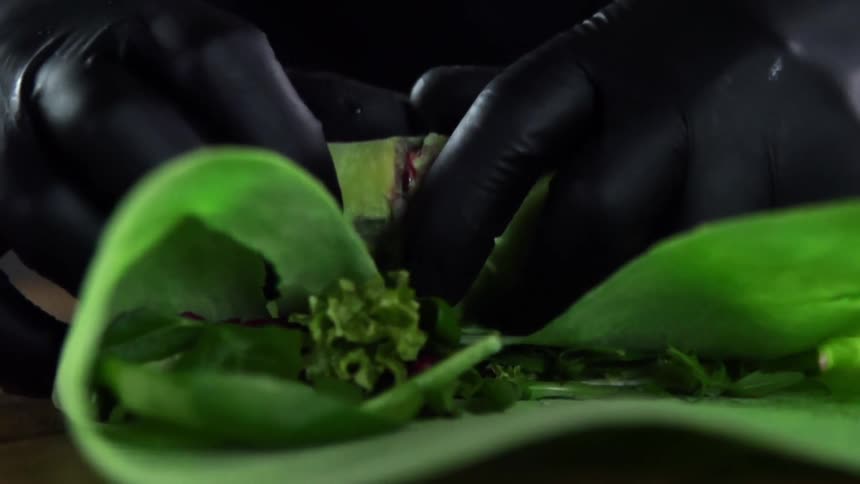 A person is rolling food into a green wrap