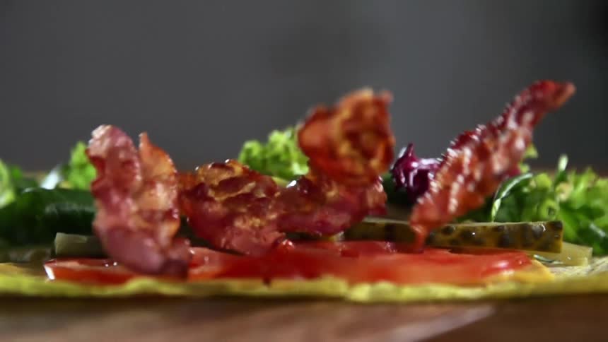 Bacon falling on to a wrap with tomatoes and pickles
