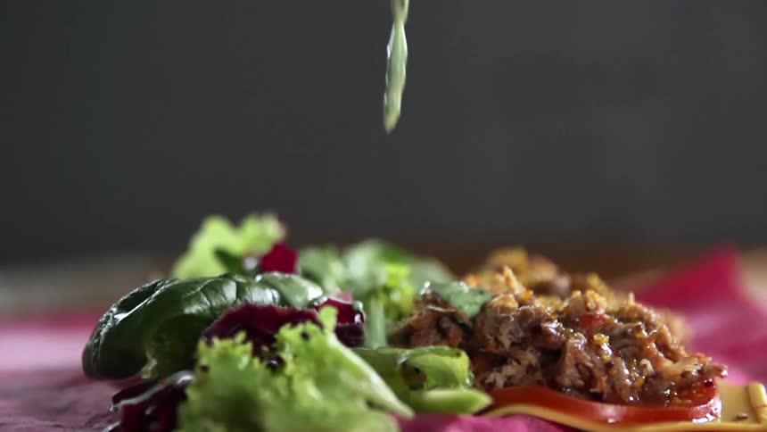 A green sauce falls onto vegetables and shredded meat lying atop a red tortilla