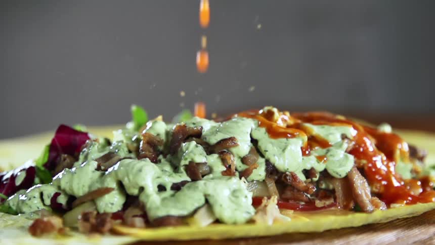 Sauce dripping over the filling of a flour tortilla on the table