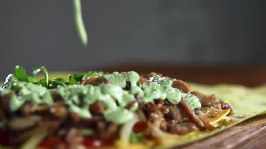 Light green sauce is gently poured over the top of pile of meat and vegetables