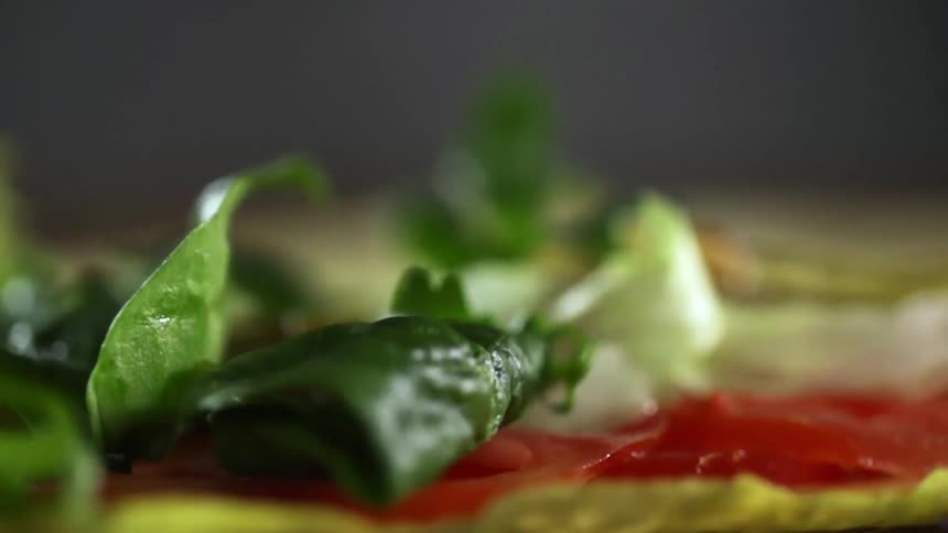 Leafy vegetables drop onto tomato slices against grey background