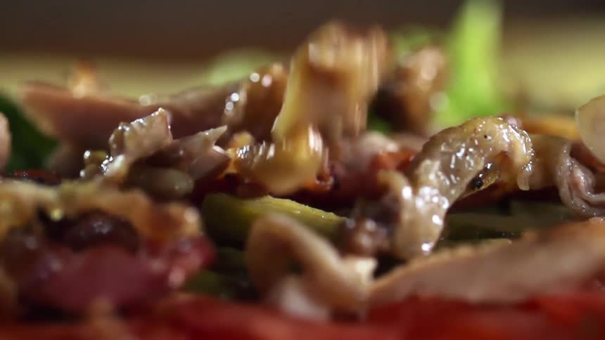 Pieces of grilled meat are dropped onto the top of an entree as it is being prepared