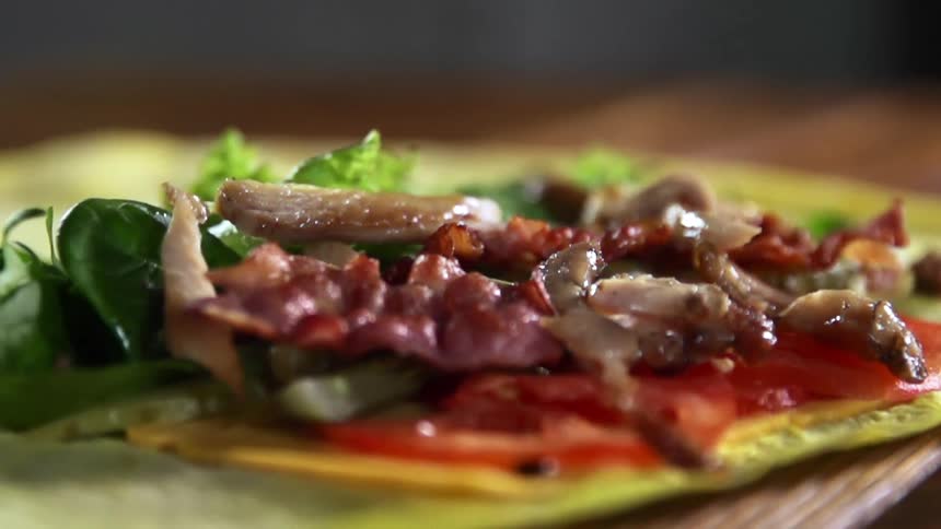 Strips of meat falling onto a tortilla covered in vegetables