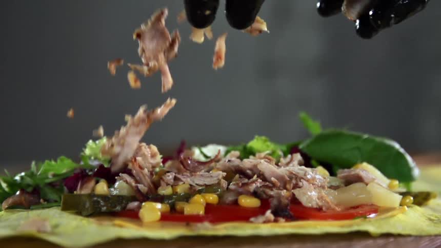 A person with black gloves tossing meat onto vegetables