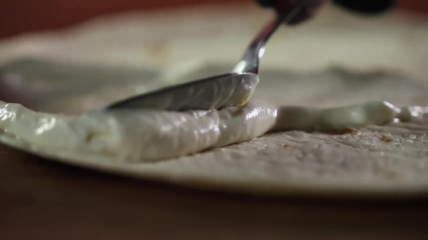 A person spreads sauce on a pizza dough