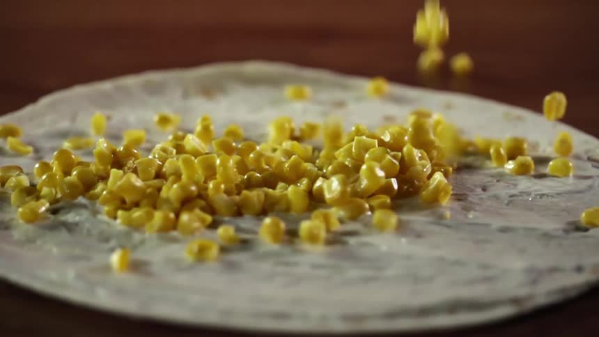 Large amount of corn kernels dropping onto a flour tortilla