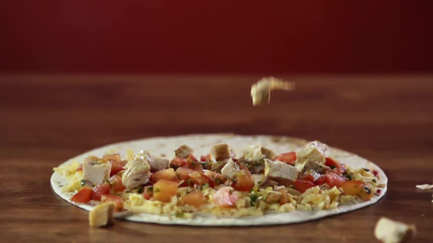 Pieces of chicken falling on vegetables on a flatbread on a table