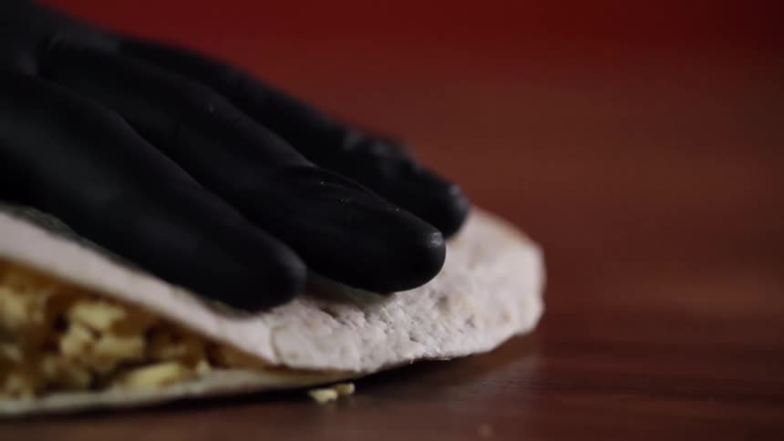 A hand covered in a black glove closes a tortilla filled with rice and vegetables
