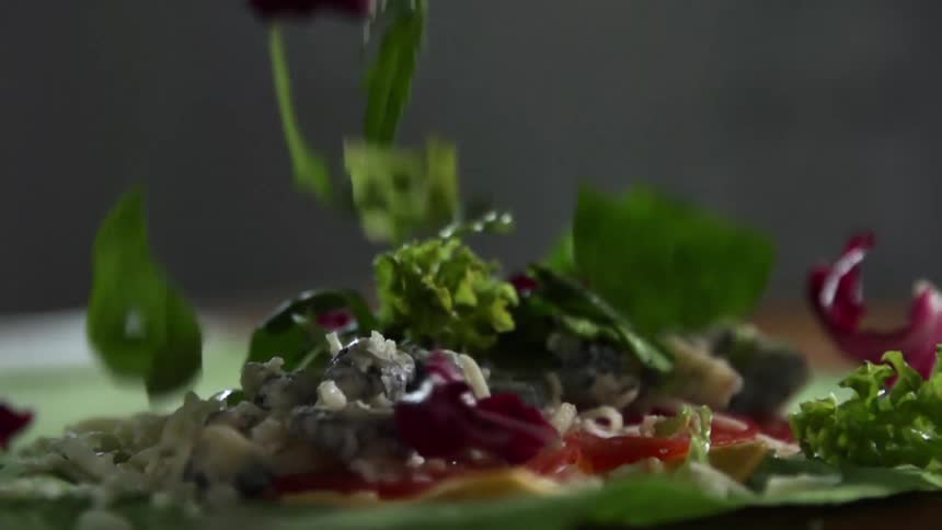 Several pieces of lettuce and spinach are dropped onto an open soft taco
