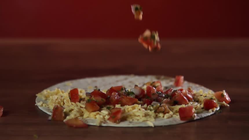 Tomatoes falling over a soft flour tortilla in a wooden table
