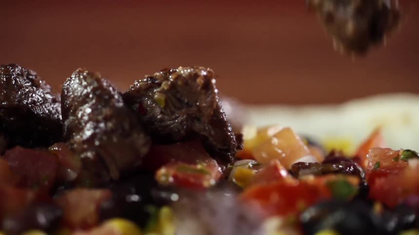 Pieces of grilled pork fall over the filling of a flour tortilla