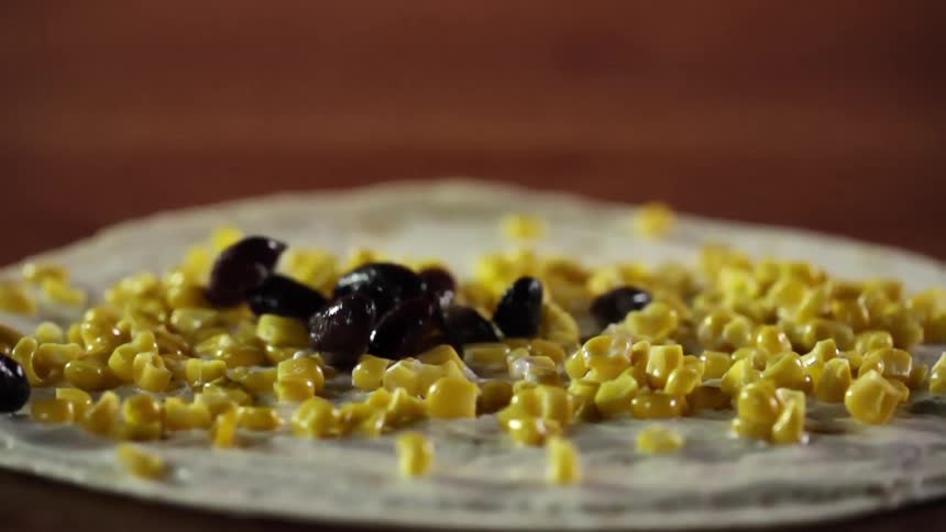 Black beans falling on a tortilla with corn on it