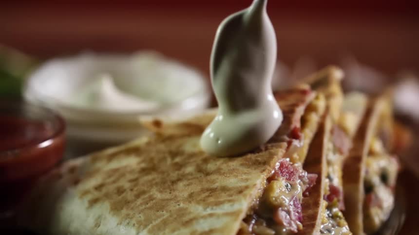 A spoon places a blob of sauce on a pita sandwich