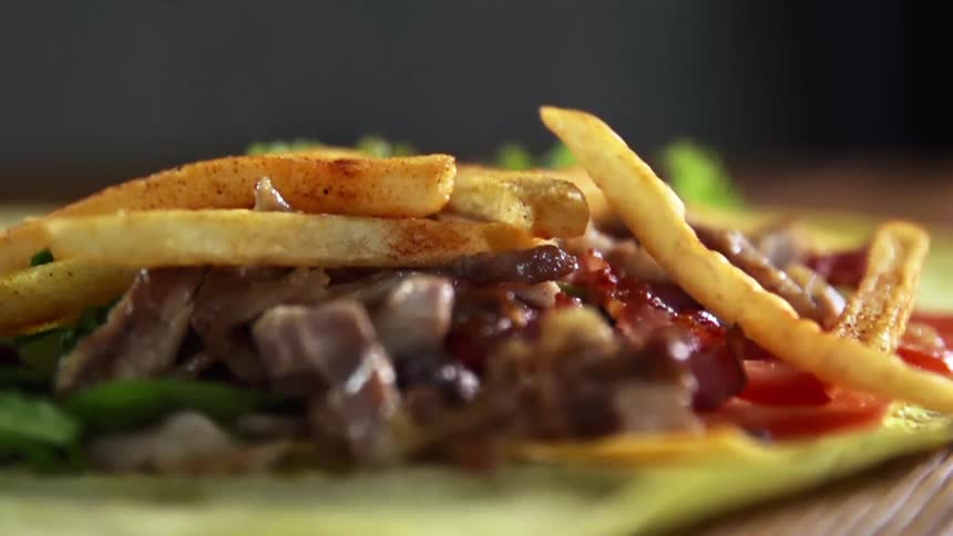 French fries fall over the meat and vegetables filling of a flour tortilla