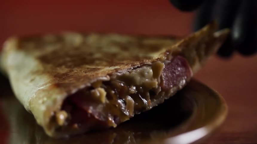 A gloved hand lays a wedge of quesadilla down on a plate