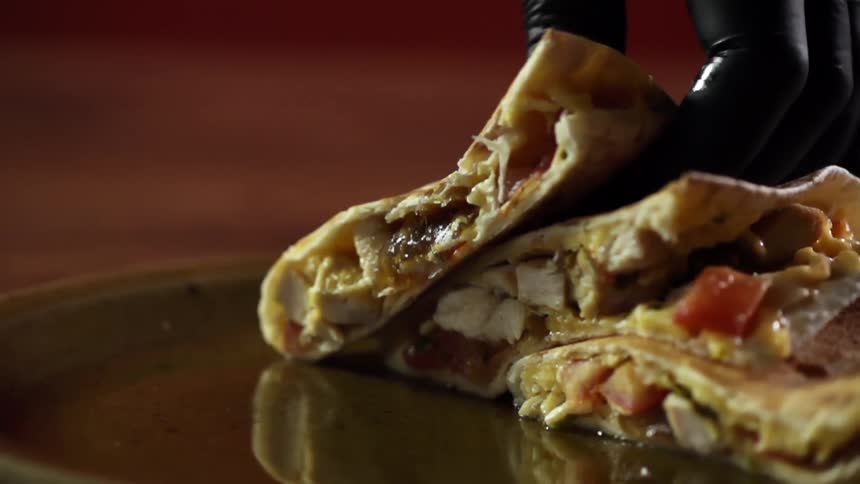 A gloved hand places a sliced quesadilla on a red plate