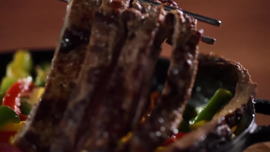 Serving steak strips using chopsticks over cooked vegetables inside a cast iron pan