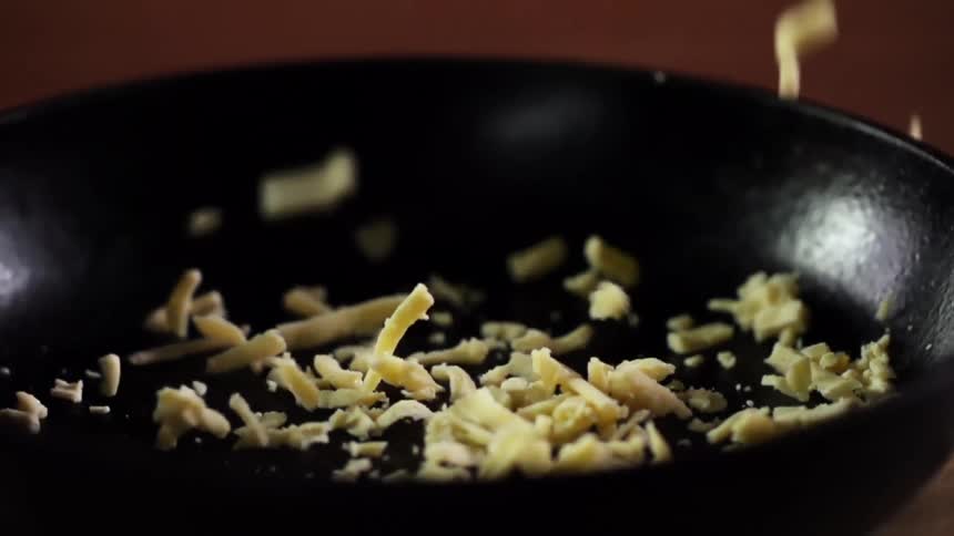 Grated white cheese falls inside a cast iron pan over a wooden table