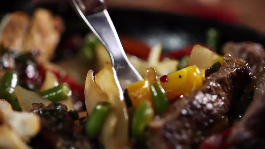 A fork being placed into a bowl with vegetables and meat