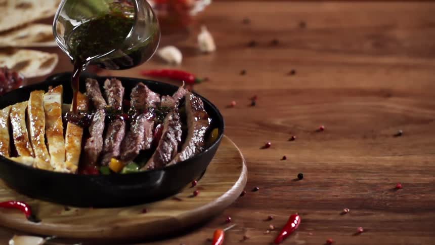Sauce being poured onto steak and chicken and vegetables in a pan