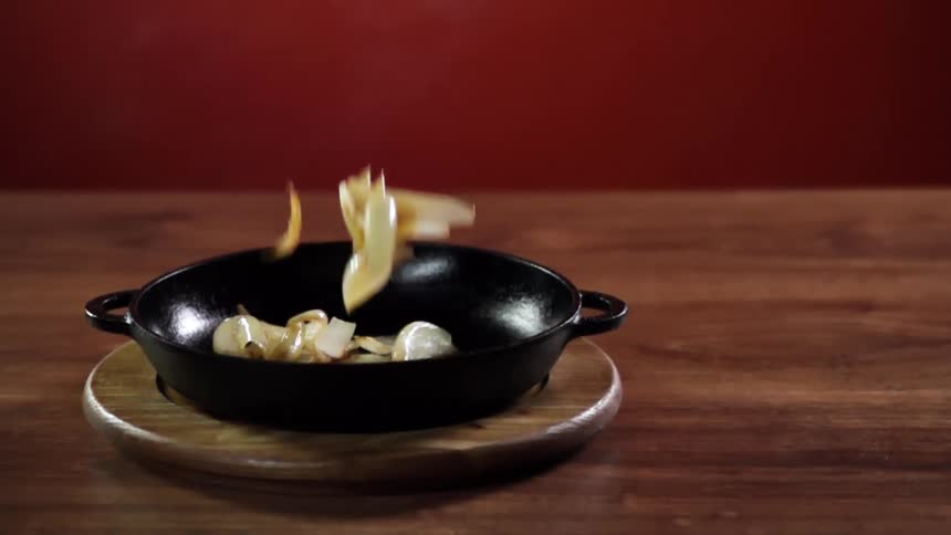 Several slices of cooked onion are dropped into a dark metal pan