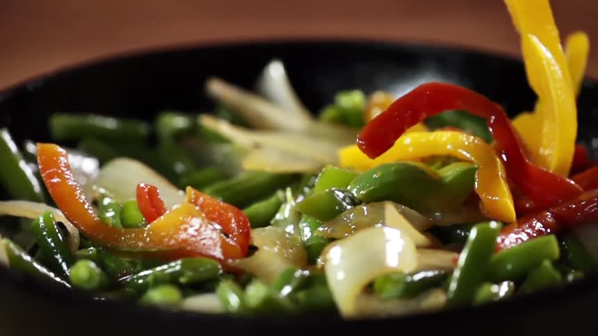 Pan roasted vegetables are lightly sauteed in olive oil and are being dropped into a black skillet