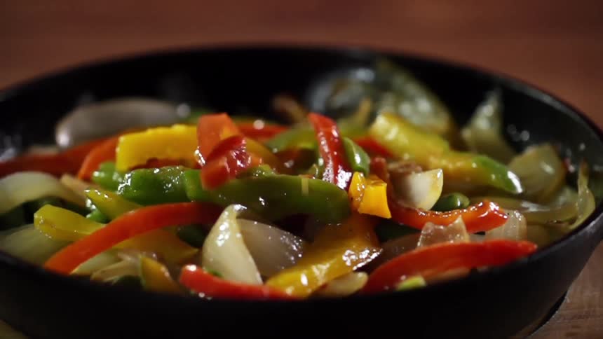 Bell peppers are added to onions in cast iron skillet resting on wooden disk