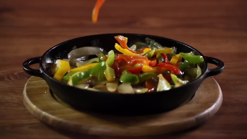 Sliced colorful peppers are dropped down onto a bed of sauteed onions in a cast iron pan with handles