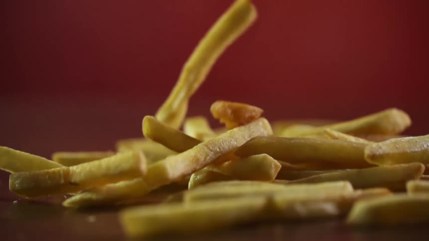 French fries being dropped onto a red backdrop in a studio