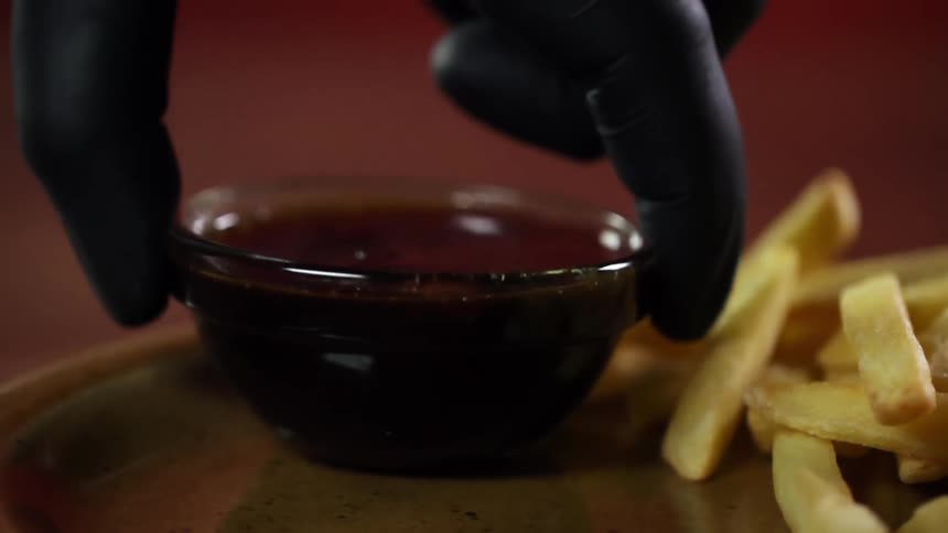 A dipping bowl being placed on a dish next to a pile of french fries