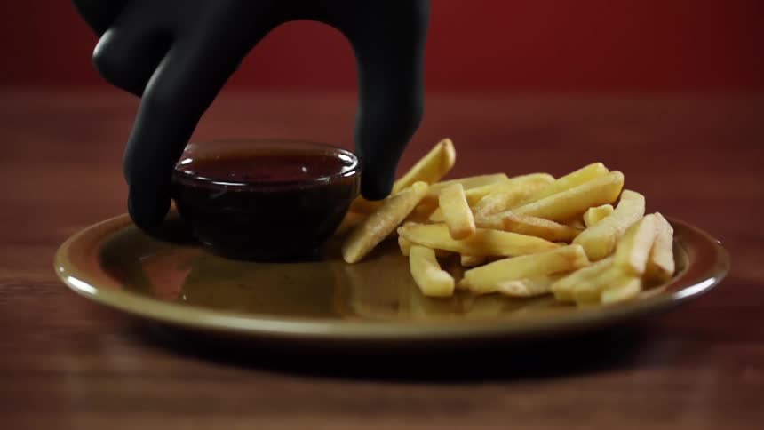 Chef wearing black latex gloves places a small bowl of sauce next to french fries in a plate
