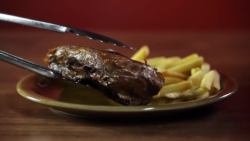 Ribs being placed on a plate with fries and dipping sauce on a table