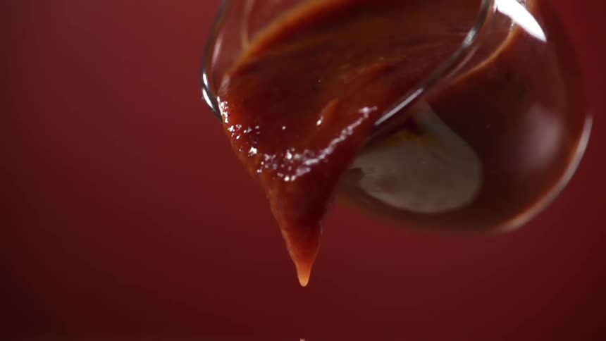 Red sauce pouring out in slow motion from a glass cup